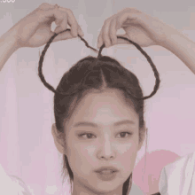 a woman is braiding her hair into a bun and making a heart shape with her hands .