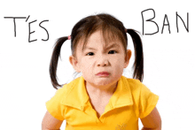 a little girl in a yellow shirt stands in front of a sign that says ban