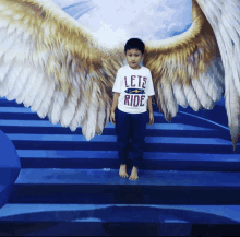 a boy wearing a lets ride shirt stands in front of a painting of wings