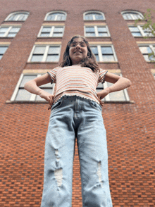 a girl is standing in front of a brick building with her hands on her hips