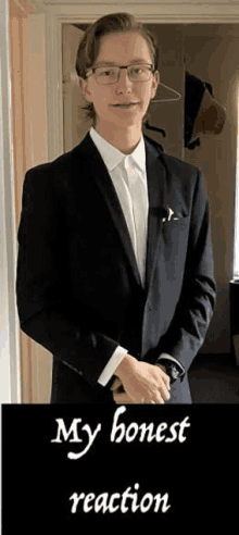 a young man in a suit and tie is standing in a hallway with his hands folded .