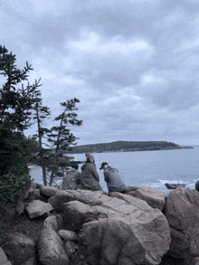 two people sitting on rocks overlooking the ocean