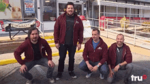 four men are posing for a picture in front of a store with a sign that says " low prices "