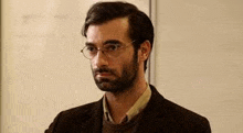 a man with a beard wearing glasses and a suit is standing in front of a whiteboard .