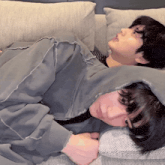 two people laying on a couch with one wearing a grey sweatshirt