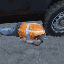 a man wearing an orange vest is laying on the ground next to a tire that says " infected " on it