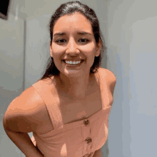 a woman in a pink tank top is smiling for the camera while standing in front of a white wall .