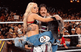a man is carrying a woman in a wrestling ring with a crowd watching .