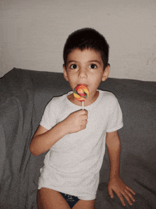 a young boy sitting on a couch eating a rainbow lollipop