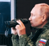 a man in a military uniform is looking through binoculars with a russian flag patch on his sleeve