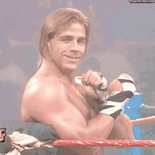 a man without a shirt is sitting in a wrestling ring with his arms crossed and smiling .