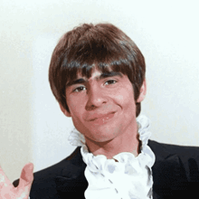 a young man wearing a tuxedo and a white ruffled collar smiles for the camera