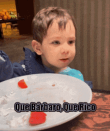 a little boy is sitting at a table with a plate of food and the words que barbaro que rico on the bottom