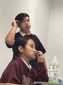 a boy and a girl sit in a classroom with a bottle of water in front of them