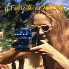 a woman wearing heart shaped sunglasses is taking a picture with a polaroid camera with the words feliz ano 2023 written above her