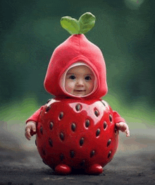 a baby is wearing a strawberry costume with a leaf on top .