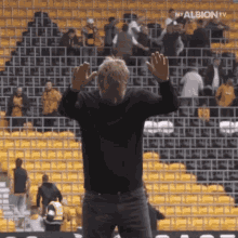 a man stands in front of a crowd in a stadium with the words my albion tv on the bottom left