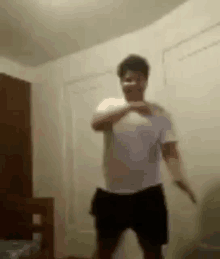 a man in a white shirt and black shorts is dancing in a room in front of a door .