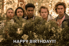 a group of people standing in front of a bush with the words happy birthday written below them