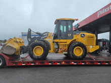 a yellow deere tractor is parked in front of a gas station