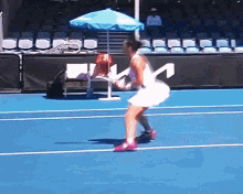 a woman in a white dress is playing tennis on a blue court with the letter m on the side