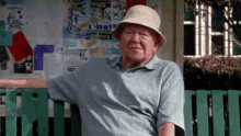 an elderly man wearing a hat is sitting on a bench in front of a sign that says ' sydney '