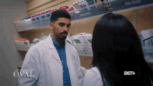 a man in a lab coat is talking to a woman in a pharmacy with the oval written on the bottom