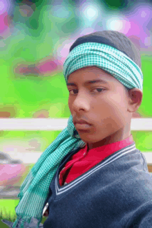 a young boy wearing a green and white head scarf looks at the camera