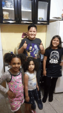 a boy wearing a star wars shirt gives a thumbs up with two girls