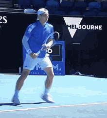 a man in a blue shirt and white shorts is holding a tennis racquet on a tennis court in front of a melbourne sign