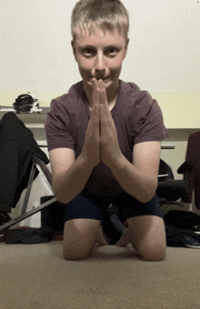 a young boy is kneeling down with his hands folded in prayer