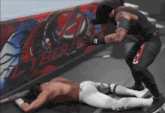 a wrestler is laying on the ground while another wrestler stands nearby