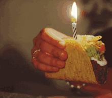 a person holding a taco with a lit candle on top