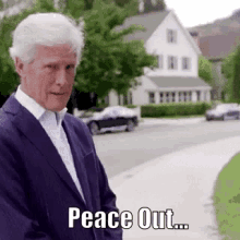 a man in a purple suit and white shirt is standing on a sidewalk with the words peace out written on it .