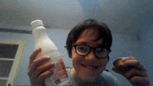 a young boy wearing glasses is holding a bottle of milk and a cookie