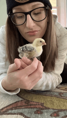 a woman with glasses is holding a small chicken in her hands