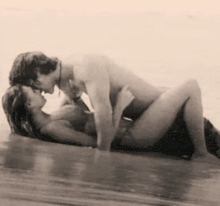 a man and a woman are kissing in the water on a beach .