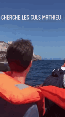 a man wearing an orange life jacket looks out over the ocean with the words cherche les culs mathieu above him