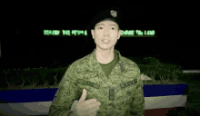 a man in an army uniform salutes in front of a sign that says " serving the people securing the land "