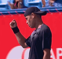 a man wearing a hat and a wristband is standing on a tennis court with his fist in the air