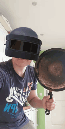 a man wearing a helmet holds a frying pan in front of his face