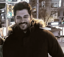 a man with a beard wearing a black jacket with a fur hood is smiling