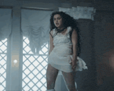 a woman in a white dress is standing next to a window