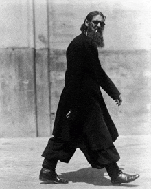 a man with a beard wearing sunglasses and a black coat is walking down the street