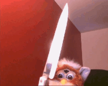 a furby is holding a large knife in front of a red wall .