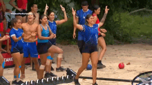 a group of people are standing on a sandy beach and one of them is giving the peace sign .