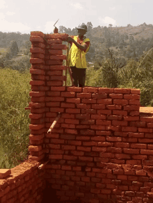 a man wearing a hard hat is working on a wall of bricks