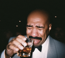 a man with a mustache is crying while holding a shot glass of whiskey