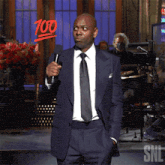 a man in a suit and tie holds a microphone in front of a snl logo