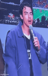 a young man in a purple jacket is holding a microphone and talking into it .